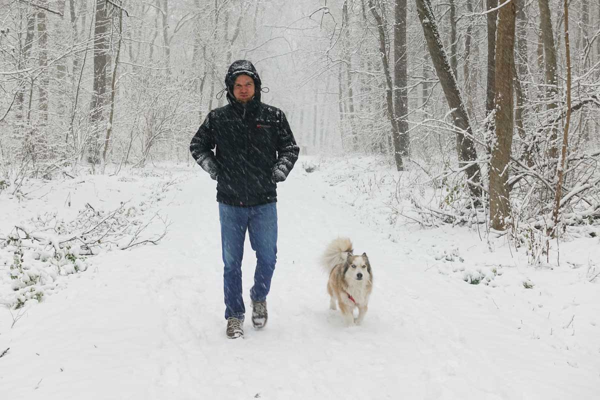 Man and his dog walking through snow in wood