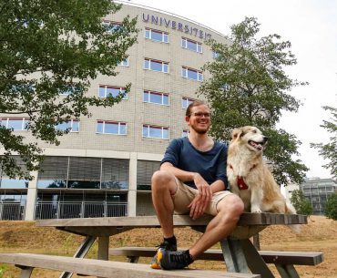Student sitzt mit Hund vor der Universität Maastricht